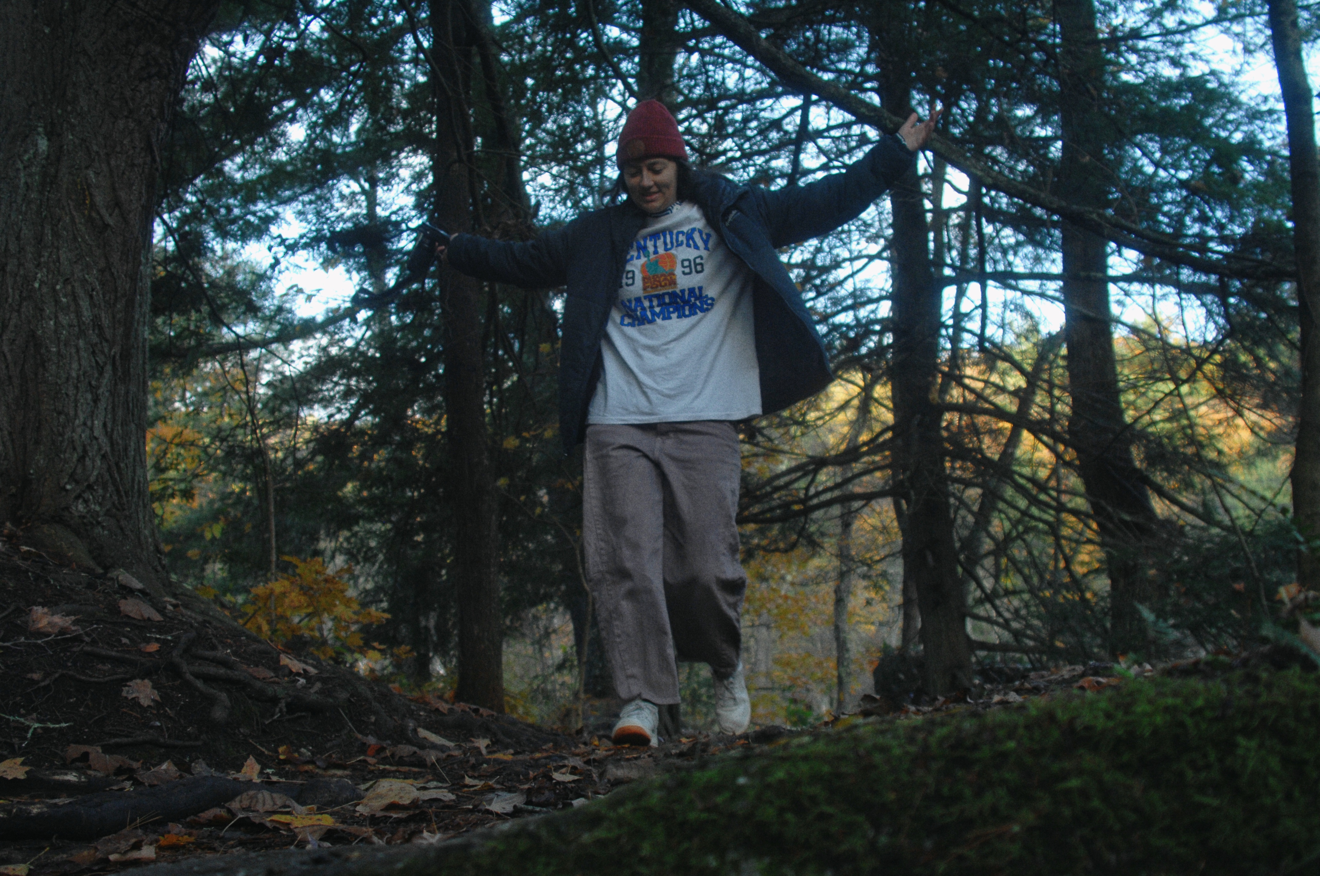 A woman prancing down a hiking trail surrounded by green pine trees and shadows.